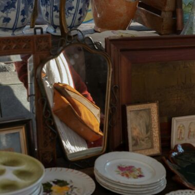 Antique market stall featuring vintage plates, porcelain vases, and a decorative mirror reflection.
