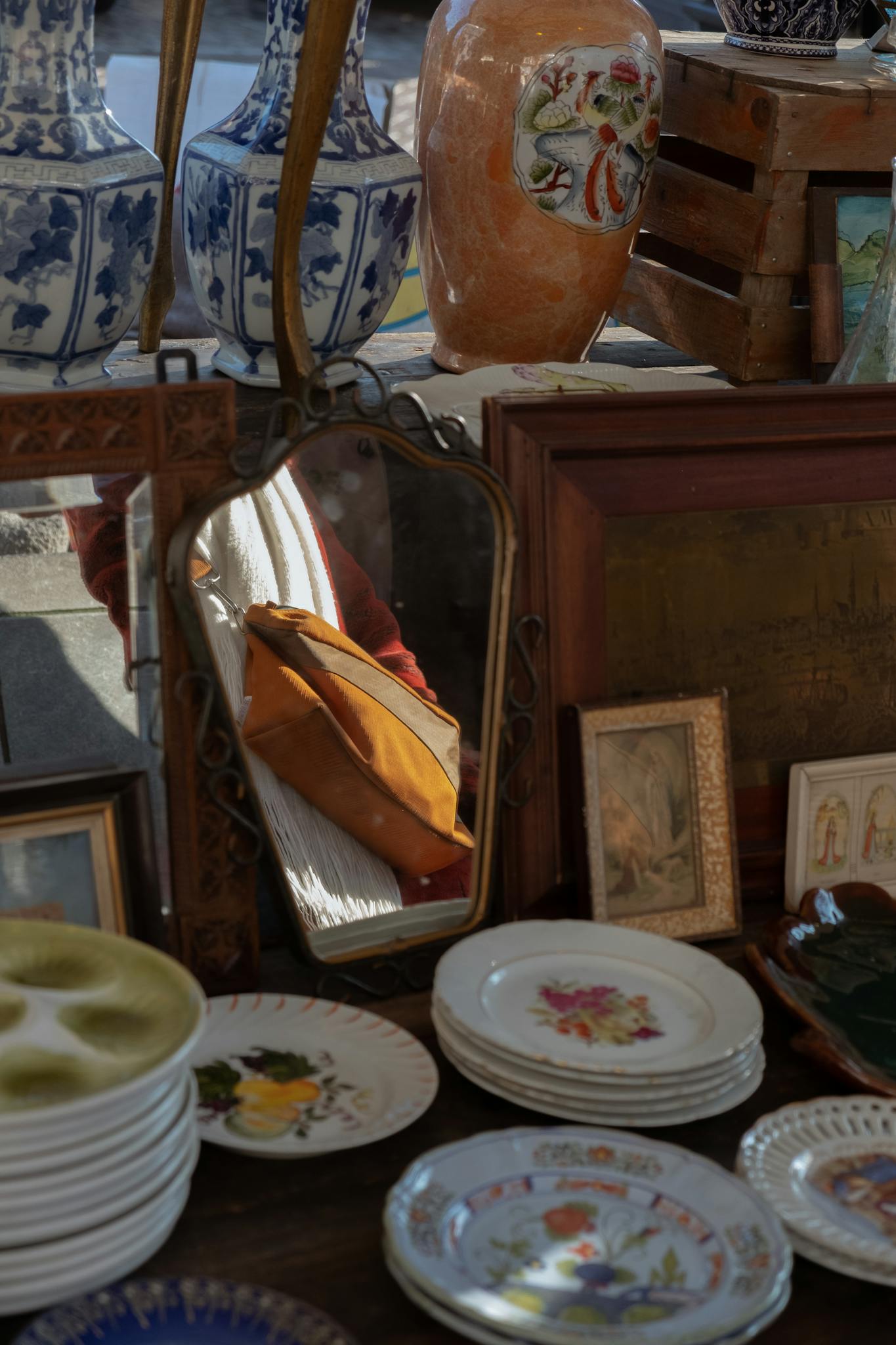 Antique market stall featuring vintage plates, porcelain vases, and a decorative mirror reflection.