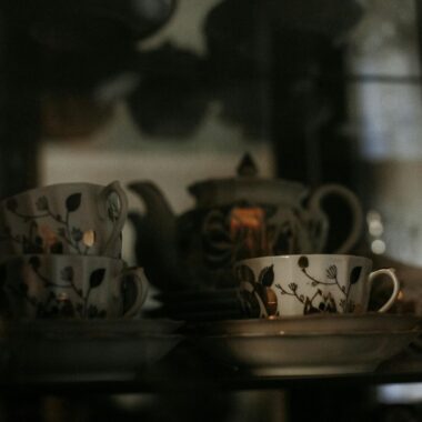 Artistic shot of a vintage porcelain tea set with intricate design in a dimly lit display cabinet.