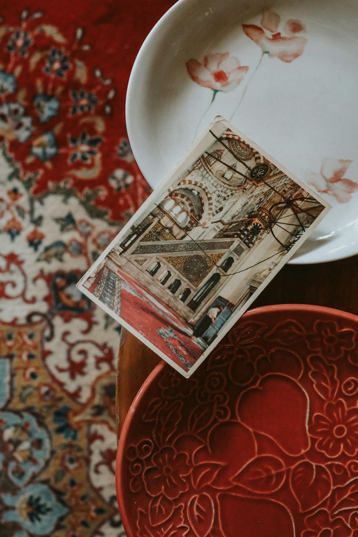 Close-up of a vintage postcard on an ornate carpet with colorful ceramic dishes.