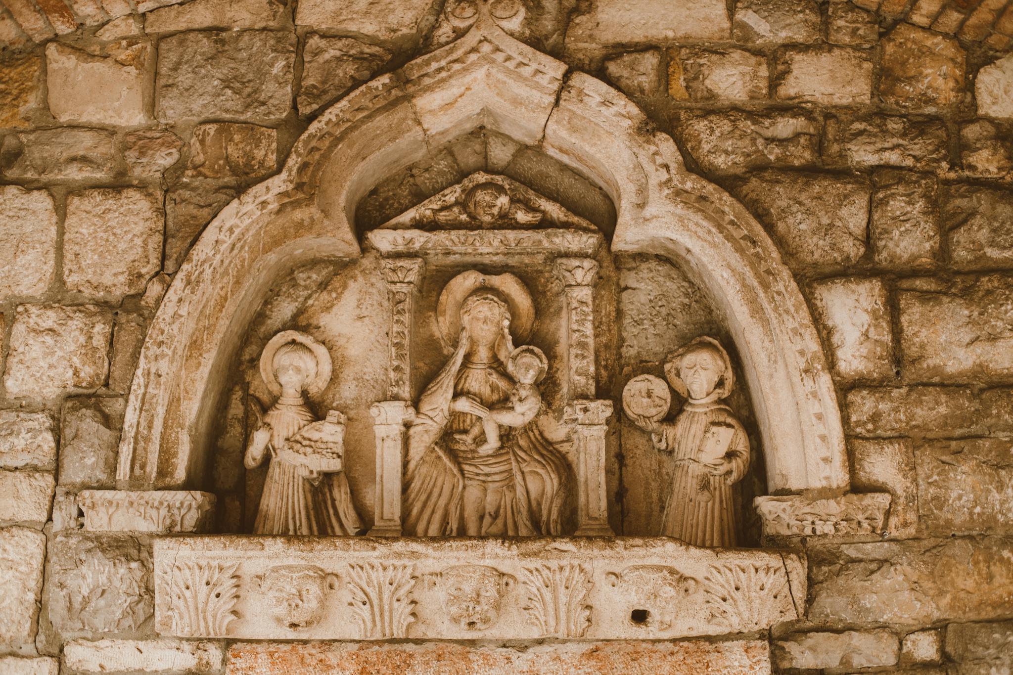 Close-up of detailed stone carving on a historical stone wall depicting religious figures.