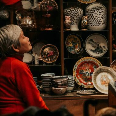 Elderly person with gray hair surrounded by traditional pottery in an artisan shop.