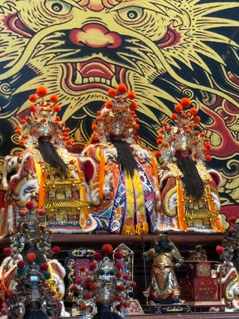 Three Gu Gong San Wang figures before a painted tiger backdrop