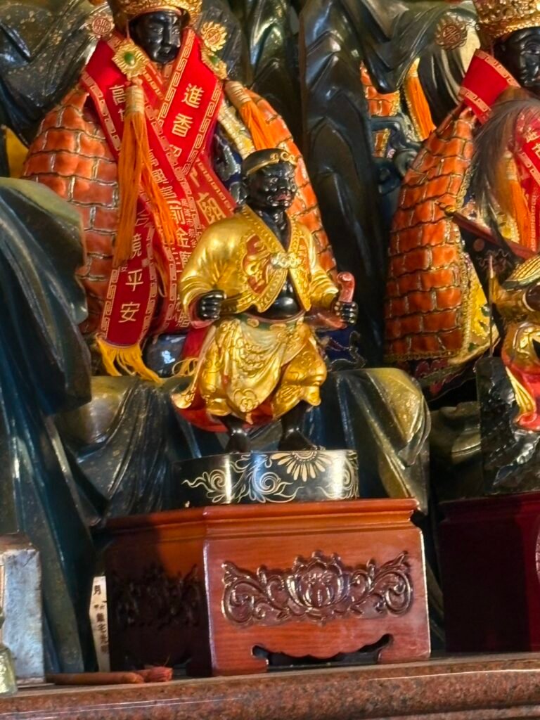 Black-faced seated deity figure in gold robes before a larger altar image