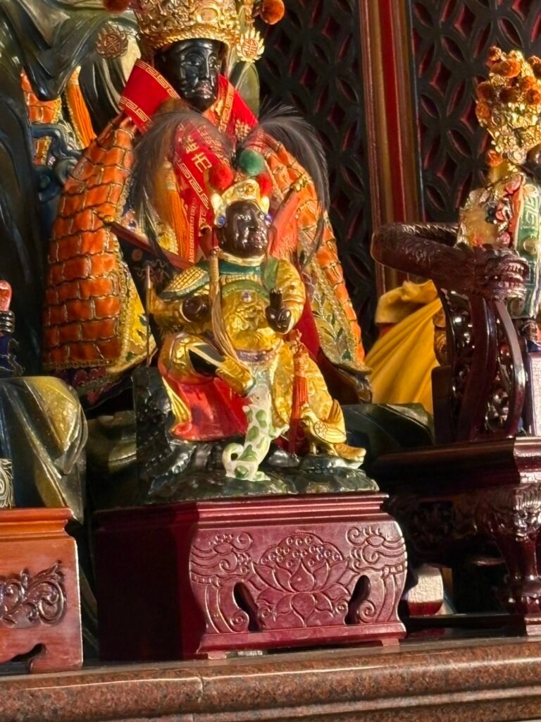 Black-faced warrior deity figure holding a sword on a carved pedestal