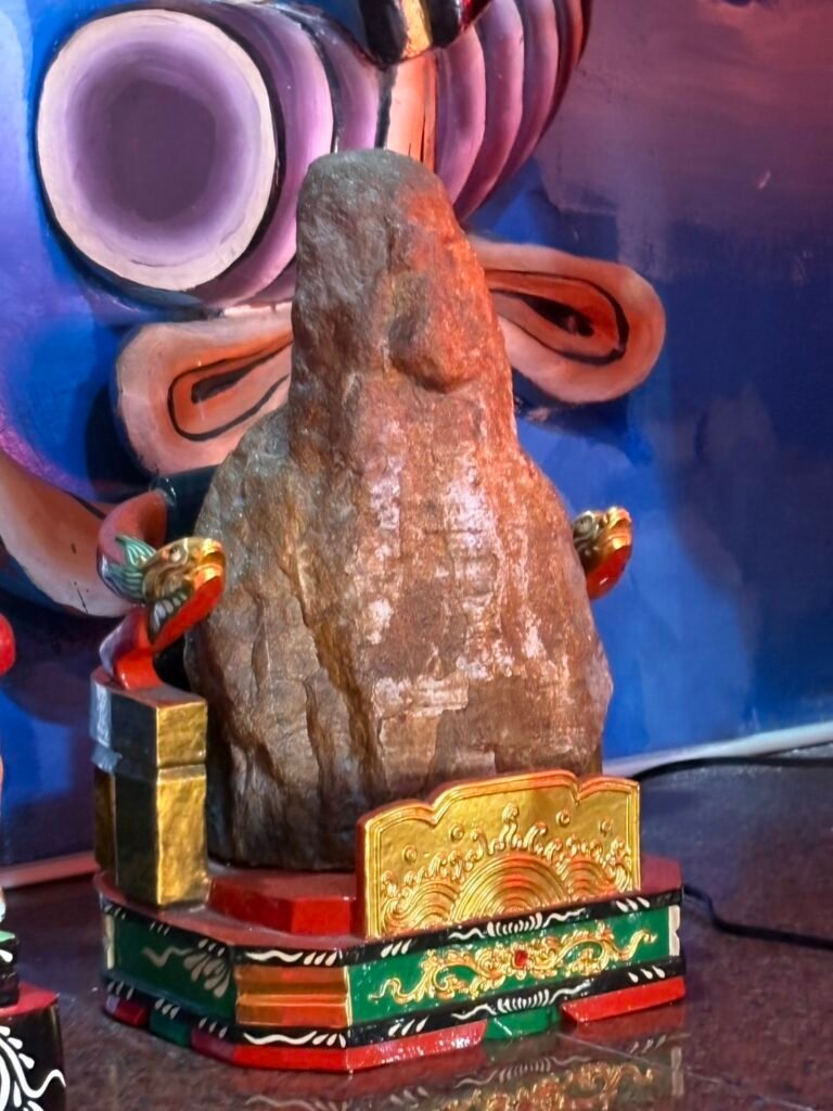 Side view of the naturally shaped Earth God stone on its painted throne